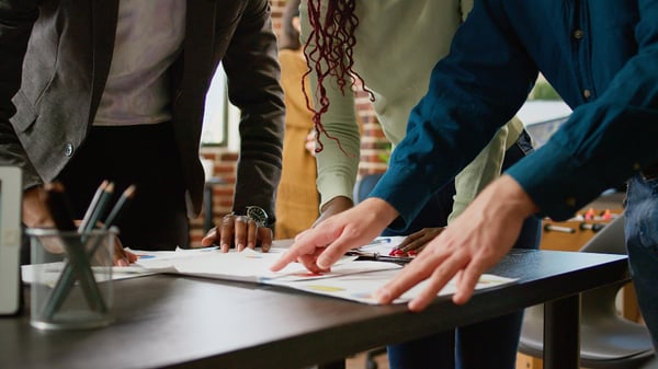 Photo shows 3 people looking at charts on a table. Photo helps illustrate article on what is market research.