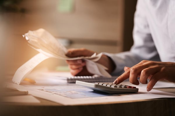 Photo from article on side hustle ideas to make extra money online show a person sitting at a table, holding receipts and using a calculator.