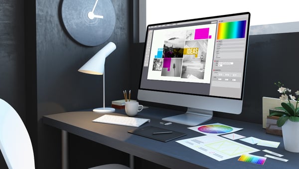 Photo shows a modern office desk, with a computer on top of it. There is a keyboard, a lamp and some pieces of paper with color palettes on top of the desk. Photo is part of the blog post titled What is branding?