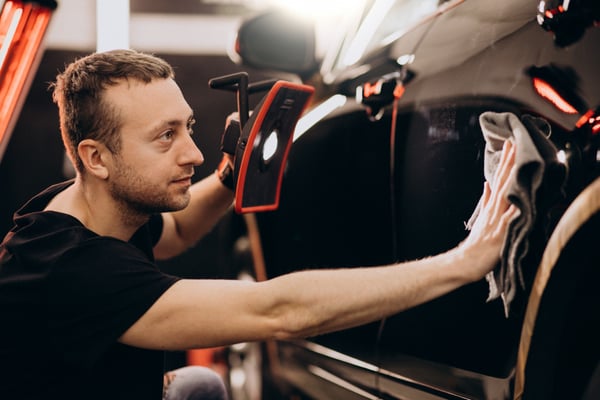 Photo shows a white man polishing a black car. This photo illustrates how car detailing can be a side hustle idea.