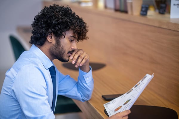 A man sits at a table and look at a piece of paper, alluding to the process of choosing the best dropshipping products.