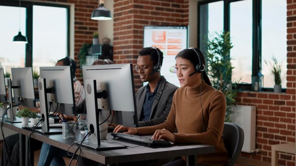 Photo shows four people sitting next to each other, working on the computer and wearing headsets. This photo illustrates the importance of customer service when learning how to sell on Amazon.