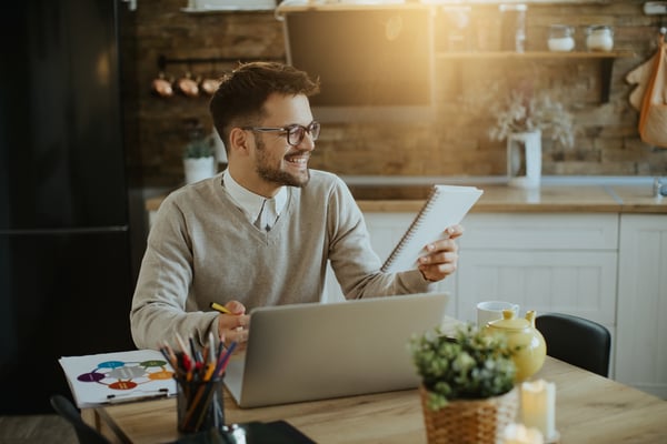 A financial advisor working at home while holding a paper and typing on his keyboard, representing that we can work at home and earn money.