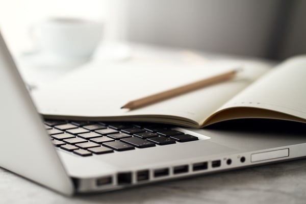 A notebook and a pencil over a laptop keyboard represent blogging as way to make a few extra dollars.