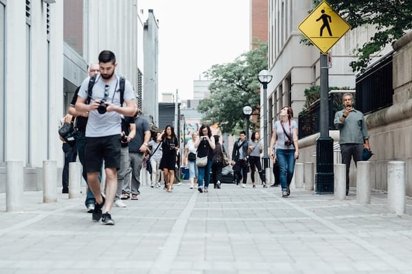 Photo shows several people walking towards the camera on the street. Many of them are holding cameras or phones. This photo illustrates the traffic you can get if you find an audience to sell enamel pins online.