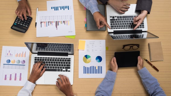 Photo shows four people sitting at a table with their laptops and some graphs and charts printed on paper, alluding to finding a target audience.