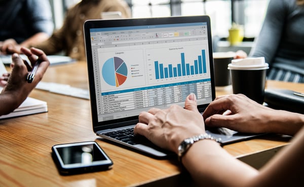 A person using a computer, looking at a research dashboard, with charts, sheets and other data, representing a market research