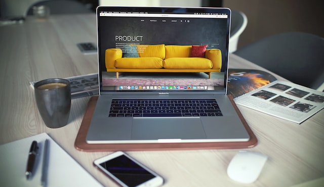 Photo shows a laptop on a table, surrounded by a coffee mug, a phone and a notepad. On the laptop screen, there is a sample online store. This is an example of how to start an online business in Canada.