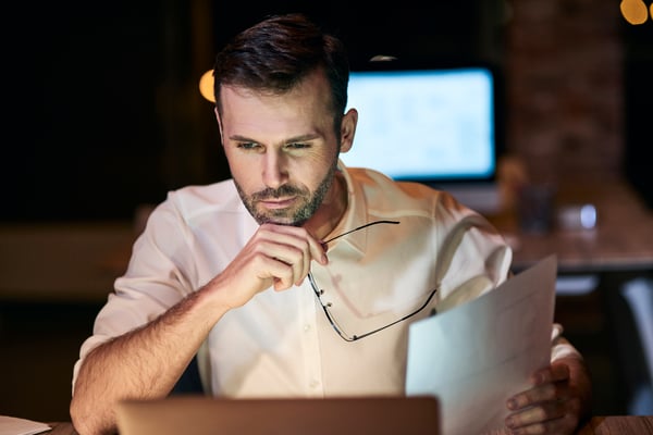 A guy holding a paper and glasses while working on a computer as freelancer, one of the ways you can make money online in canada