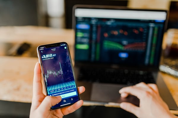 Photo from blog post on passive income ideas shows person checking stock market on phone and on their laptop