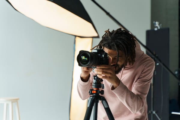 Photo of article about side hustle ideas shows a man, wearing dreadlocks and a pink hoodie, standing behind a camera in a studio.