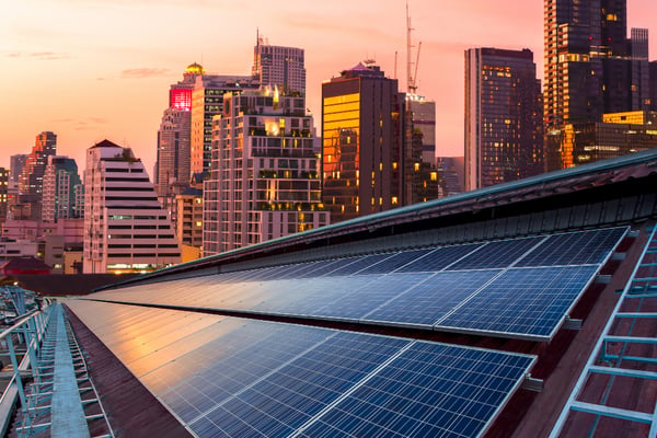 Photo from article on green marketing shows a series of solar panels, installed on the top of a building in a big city. In the background, there are several buildings and the sun is about to set.