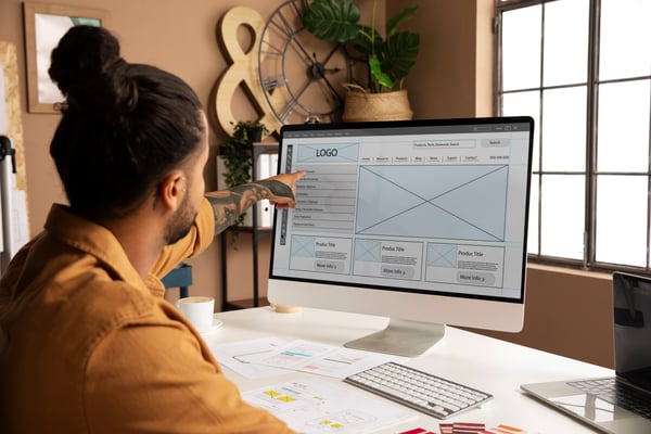 A guy pointing to a computer screen while he's developing designs and earning money at home office.