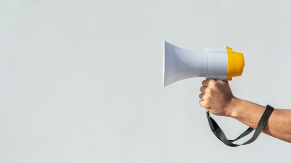 Hands holding a white and yellow megaphone pointed to the left, representing the way we want to spread our mission statement to the world.