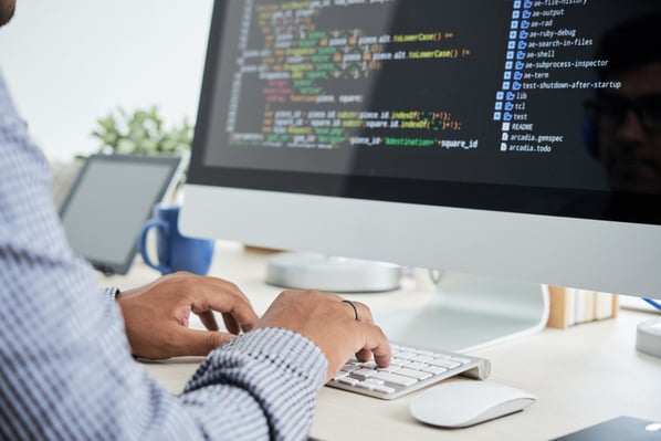 Photo that illustrates blog post on digital products to sell online shows a person sitting at a desk, typing into a computer. The monitor screen shows the person is coding.