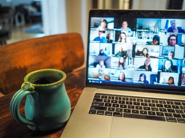 Picture that illustrates article on starting an online business in Canada shows a laptop on a wooden table, next to a ceramic mug. On the laptop screen, there are several people participating in a video call with their cameras on.