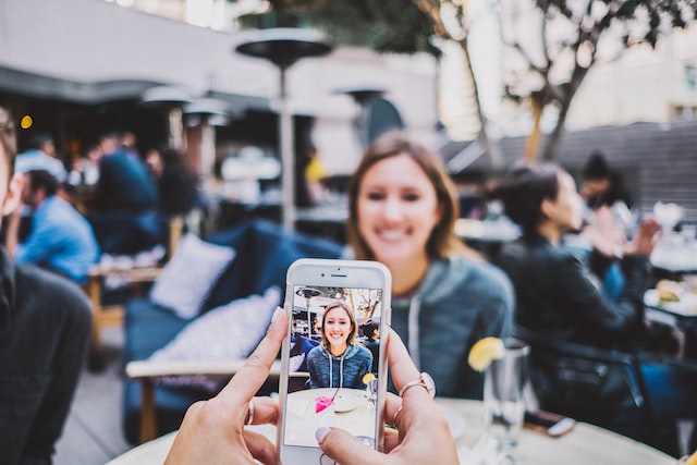 This photo represents working as a social media manager to start an online business in Canada. In the photo, there is a person sitting in a bar, and in the foreground there is someone else taking a picture of them with their phone.