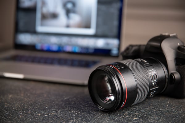 Photo shows a professional camera from up close, and in the background there is a laptop with a picture being displayed on the screen. Photo illustrates Shoplazza's blog post about digital products to sell online.