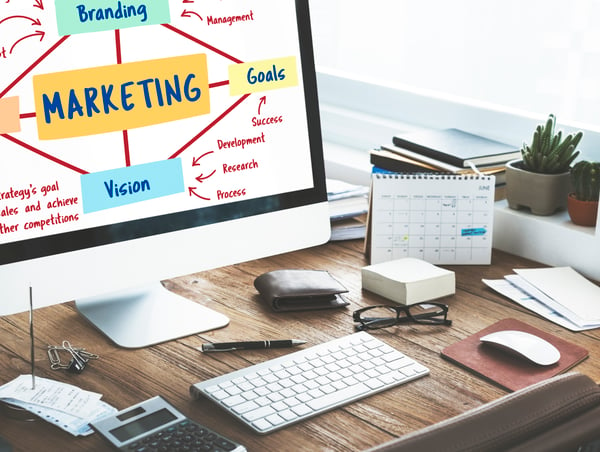 A office table filled with pens, glasses, papers, calendars and a computer with a marketing presentation on the screen. The image represent TikTok Ads planning