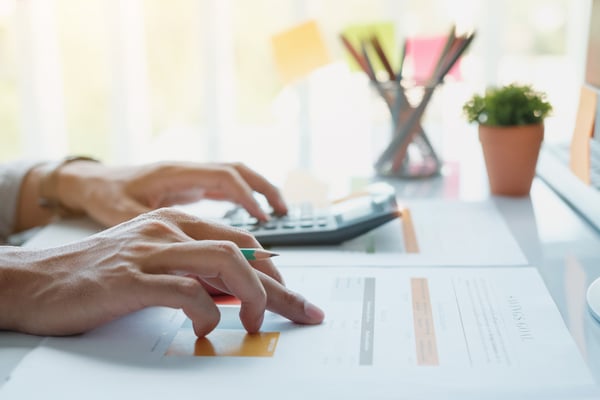 Photo of the article What is ROI shows a person's hands over a desk. One hand is using a calculator and the other is pointing at a table on a sheet of paper.